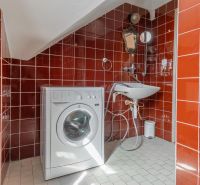 A bathroom in a cottage with red tiles, a washing machine, and a sink.