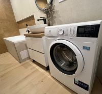 Bathroom in a 2-room apartment with a washing machine, a sink on a cabinet, and a bathtub on a floor with a wooden decor.
