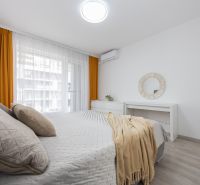 A bright bedroom with orange curtains, a bed, and ventilation in a 2-room apartment.