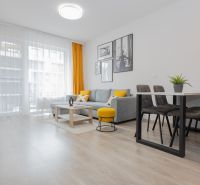 Living room in a two-room apartment with a wooden decor floor, gray sofa, and yellow accessories.