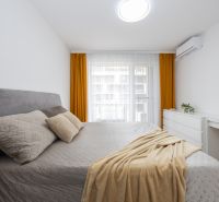 A bright bedroom in a 2-room apartment with a gray bed, ochre curtains, and white furniture.