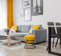 Living room with a sofa, yellow accents, wooden decor on the floor, and paintings on the wall.
