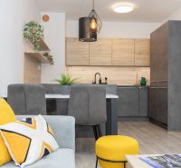 Living room with kitchen, gray furniture, yellow decorations, and wood-patterned flooring.