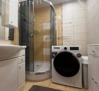 A bathroom in a 2-room apartment with a washing machine, shower, and light tiles.