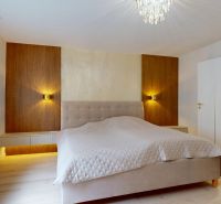A bedroom with wood-patterned flooring and spotlights in a three-room apartment.