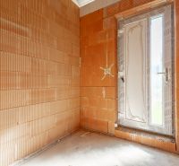 A room in an unfinished family house with brick walls and plastic doors.