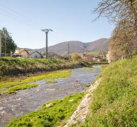 A river flowing through Drietoma past family houses with a mountain backdrop.