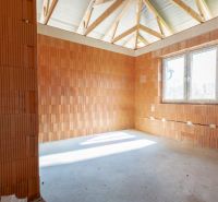 The interior of a room in a family house with wooden ceiling beams and a window.
