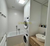 A bathroom with a washing machine, dryer, and bathtub in a 3-room apartment, light tiles, and wooden decor.