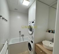 Bathroom with a bathtub, sink, and washing machine in a 3-room apartment; light tiles.