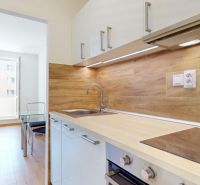 A kitchen with a wood-patterned floor in a 2-room apartment with a glass table.