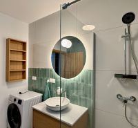A bathroom in a 2-room apartment with a sink, shower, washing machine, and wooden shelf.