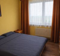 A bedroom in a two-room apartment with a wooden decor floor and orange curtains.