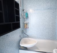 Bathroom in a 2-room apartment with a bathtub, sink, and shelving storage system.