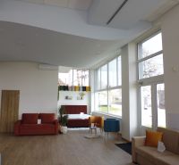 Interior of commercial spaces with wood-patterned flooring, comfortable seating, large windows.