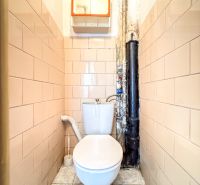 WC with beige tiles in a 3-room apartment, simple design, white toilet.