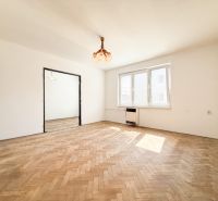 A bright room with wood-patterned flooring in a three-room apartment, large windows.