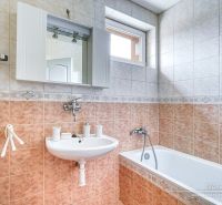 A bathroom in a family house with a sink, mirror, bathtub, and a window above the door.
