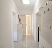 A hallway of a family house with white walls and a light floor, hooks on the wall.