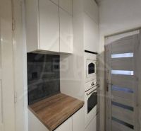 A kitchen area with white cabinets, appliances, and a wooden decor floor in a family house.