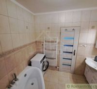 A bathroom in a family house with a bathtub, a washing machine, and a sink with a cabinet.