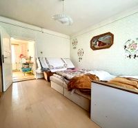 A room in a family house with a wooden decor floor, a bed, and paintings on the wall.