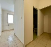 A hallway in a one-room apartment with tiled flooring, white walls, and a large window.