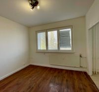 A room with a wooden decor floor in a one-room apartment, light walls, and a radiator.