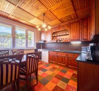 A kitchen in a family house with wooden cabinets, a colorful floor, and a view of the forest.