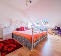 Attic room with a bed and skylights, in a family house, with a floor featuring a wooden decor.