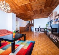 Living room of a family house with a sofa, wood-patterned flooring, and a wooden ceiling.