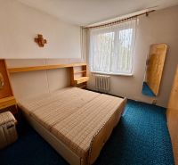 A bedroom in a 3-room apartment with a simple bed, a mirror, and a blue carpet.