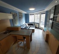 A living room with blue walls, a kitchenette, and a corner sofa in a 2-room apartment.