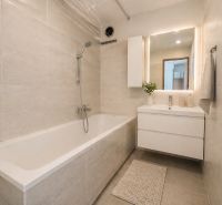 Bathroom in a 2-room apartment with a bathtub, sink, and light tiles.