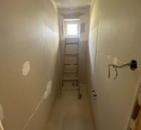A narrow room in a family house with a ladder and raw walls.