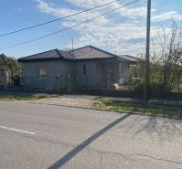 A family house in Encs with double roofs and a garden, surrounded by a fence.