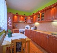 A kitchen with wooden decor, flowers on the table, and green walls in a family house.