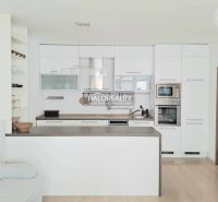 A kitchen with white cabinets and built-in appliances in a 2-room apartment, with a wood-patterned floor.