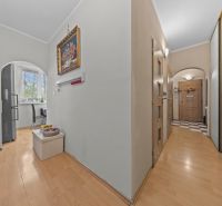 A hallway in a 3-room apartment with a wooden decor floor, a kitchen seen through an arch.