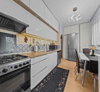 A kitchen with a stove, white cabinets, and a wooden decor floor in a 3-room apartment.