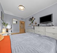 A bright bedroom with a bed, television, decorations, and wood-patterned flooring in a three-room apartment.