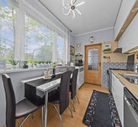 A kitchen table with chairs, plants on the windowsill, in a 3-room apartment, floor with wooden decor.