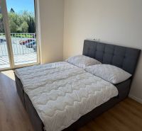Bright bedroom in a 2-room apartment with wood-patterned flooring and a French window.