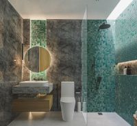 A bathroom in a villa with a mosaic green wall and dark marble tiles.
