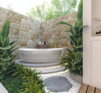 A bathroom in a villa with a freestanding bathtub, greenery, and a stone wall.