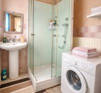 Bathroom with a washing machine, shower, sink, and carpet in a family house.