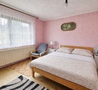 A room in a family house with a double bed, a television, and pink wallpaper.