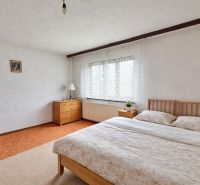 Bedroom in a family house with a wooden bed and dresser, white walls, small window.