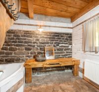 A bathroom in a family house with a stone wall, wooden ceiling, and rustic furnishings.