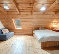 Attic room with wooden walls, a bed, and a sofa. Floor with wooden decor.